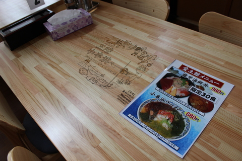 食堂内のテーブルの写真。テーブル中央にイラストが印刷されている